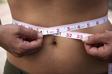 Mid section view of a woman measuring her waist with a tape measure