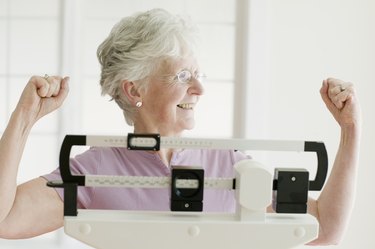 Senior woman weighing self on scale and cheering