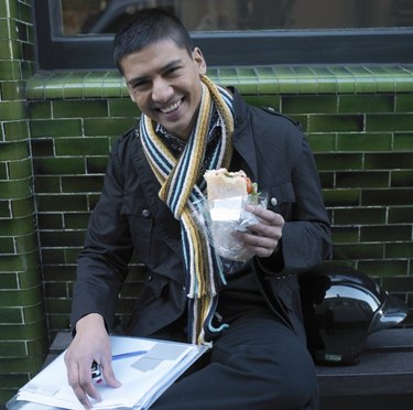 Young man sitting outside holding lunch,smiling, portrait