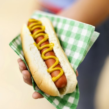 close-up of hand holding hot dog in napkin