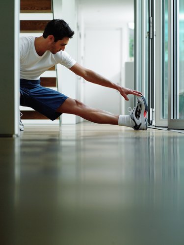 Man in sports clothes performing leg stretch in hallway, ground view