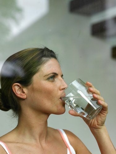 Woman drinking glass of water, view through window, close-up