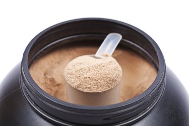 Scoop of chocolate whey isolate protein in black plastic containter