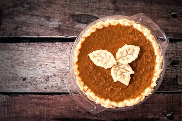 Pumpkin pie with leaf pastry toppings against rustic wood
