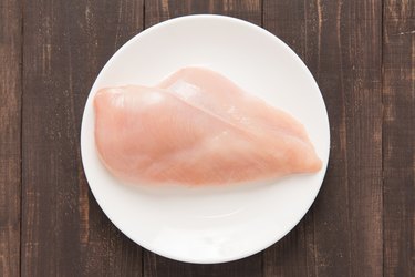 Raw chicken breast fillets on white dish.