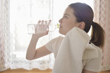Close-up photo of a woman drinking water and toweling off her face after a workout.