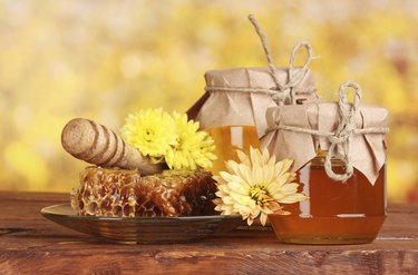 two jars of honey,honeycombs and drizzler on yellow background