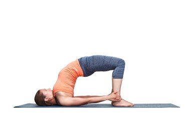 Beautiful sporty fit yogini woman practices yoga asana setu bandhasana - bridge pose advanced variation in studio isolated on white