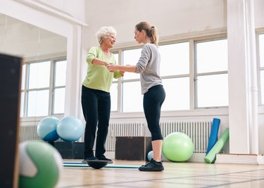 Trainer helping senior woman on bosu balance training platform