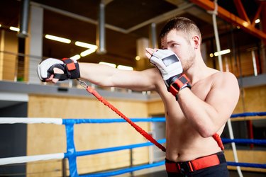 Portrait of shirtless fighter practicing straight punches with resistance band belt in boxing ring
