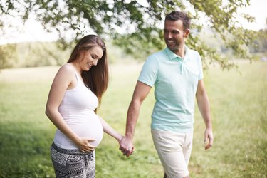 Pregnant woman with husband walking on meadow