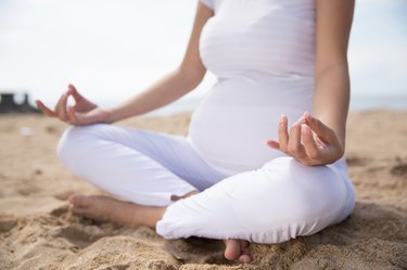 pregnant person wearing white, sitting in a cross-legged position on the beach.