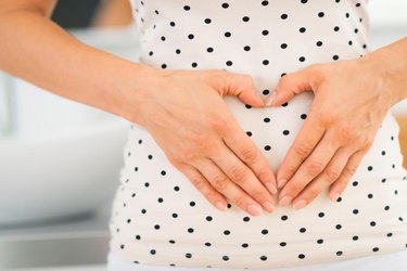 Closeup on young woman holding hands in heart shape on her belly