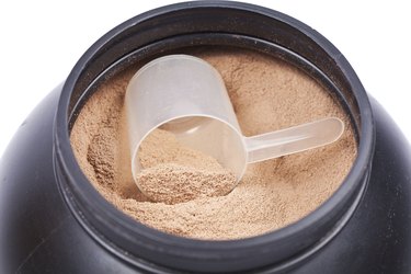 Scoop of chocolate whey isolate protein in black plastic containter