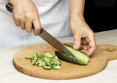 Woman's hand slicing a cucumber.