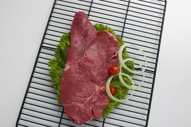 Uncooked sirloin steak on broiler grill with lettuce, onion, tomato garnish