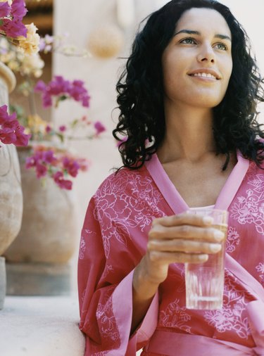 Young Woman Standing Outdoors Wearing a Dressing Gown and Holding a Glass of Water