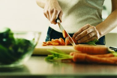 Mid Section View of a Young Woman Cutting a Carrot on a Chopping Board at a Kitchen Counter