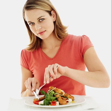 portrait of a young woman eating fried fish with a fork and knife