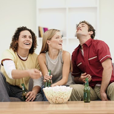 Three young people eating popcorn and drinking beer in room