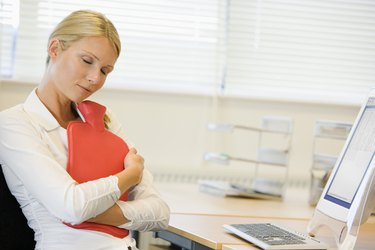 Businesswoman hugging heating pad at desk