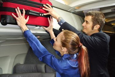Couple putting suitcase in overhead compartment