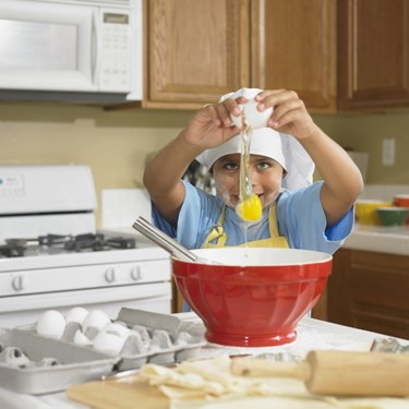 Young Hispanic boy cracking egg into bowl in kitchen