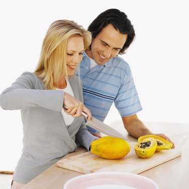 Close up of a young smiling couple cutting fruit on a chopping board