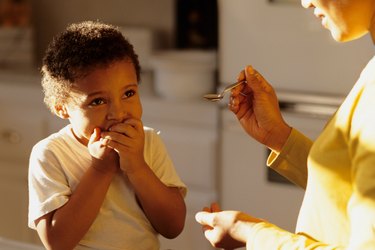 Young boy (4-5) covering mouth, refusing to take teaspoon of medicine