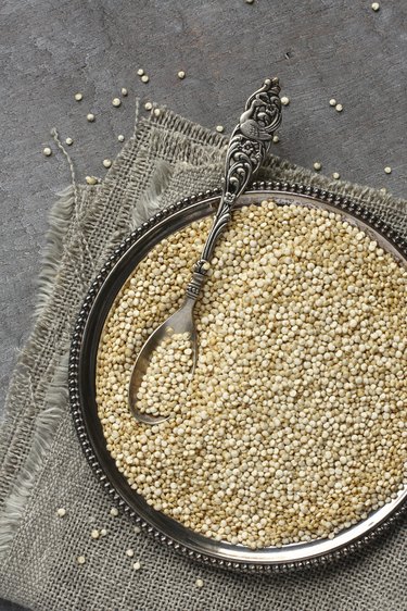 Uncooked quinoa in metal plate on wooden background