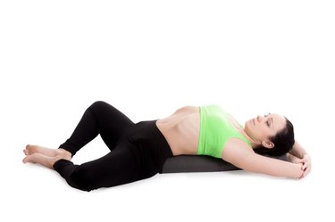 Sporty girl on white background resting in Reclining Bound Angle yoga Pose, Supta Baddha Konasana, restorative, relaxing asana, using bolster