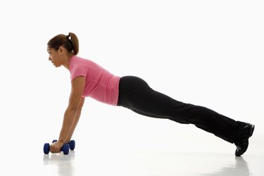 Side view of mid adult multiethnic woman wearing pink exercise shirt doing pushups while holding dumbbells.