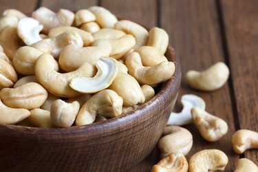 Wooden bowl of cashew nuts from above. On dark wood.