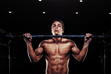 Young muscular man doing pull ups exercise on horizontal bar. Sports, fitness concept.