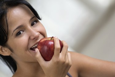 Smiling teenage girl eating apple, close-up, tilt