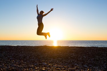 Silhouette Happy Female jumping high with arms raised beach sunrise