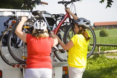 Two friends lifting bicycles from van outdoors