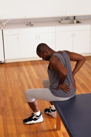 Man sitting on bed in physical therapy centre with back pain, elevated view