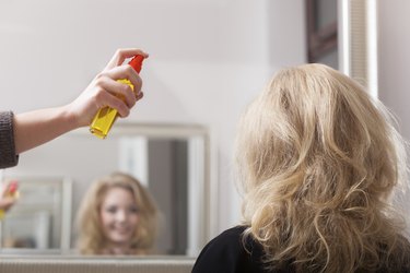 Hairstylist with hairspray and female client blond girl in salon