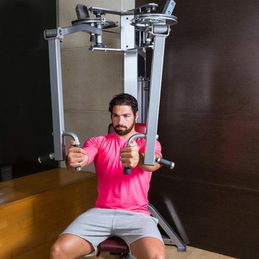 Woman trains her chest muscles on pec deck machine at the fitness