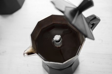 Top view of metal coffee pot with coffee in it on white table