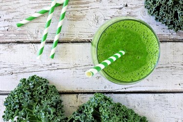 Green kale smoothie overhead view, in a glass with straw on an aged wood background