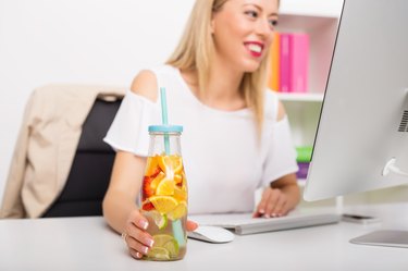 Woman at the office having re-freshening drink while working