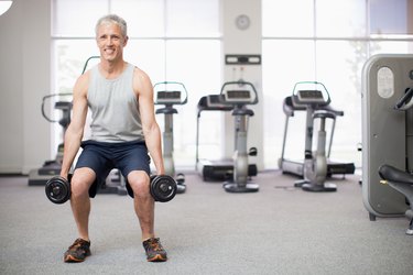Portrait of smiling man doing squats with dumbbells in gymnasium