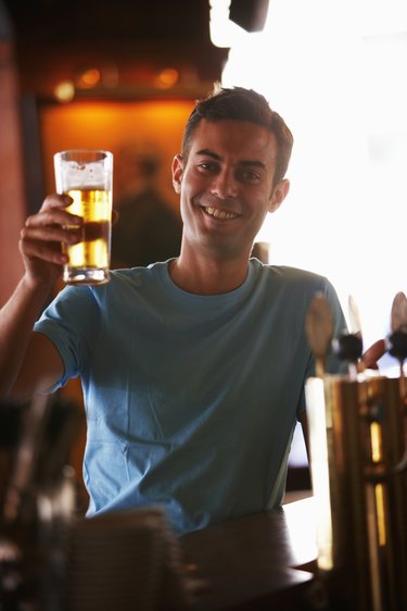 Young man holding up glass of beer in bar, smiling, portrait