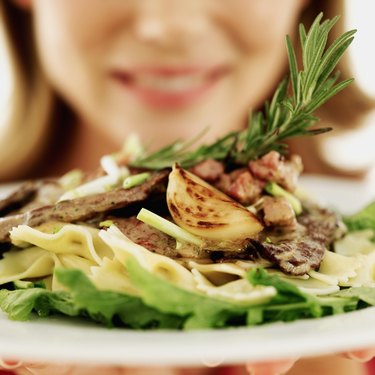 close-up of a young woman holding a plate of steak with pasta and vegetables