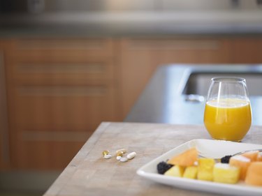 Glass of orange juice, fresh fruit and pills on kitchen counter