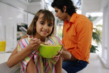 Dad with newspaper at table, girl (8-10) with bowl of cereal, portrait