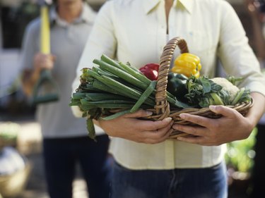 Woman holding basket of vegetables, close up, mid section