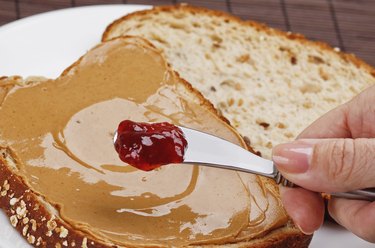 Mom spreading jelly on a peanut butter sandwich